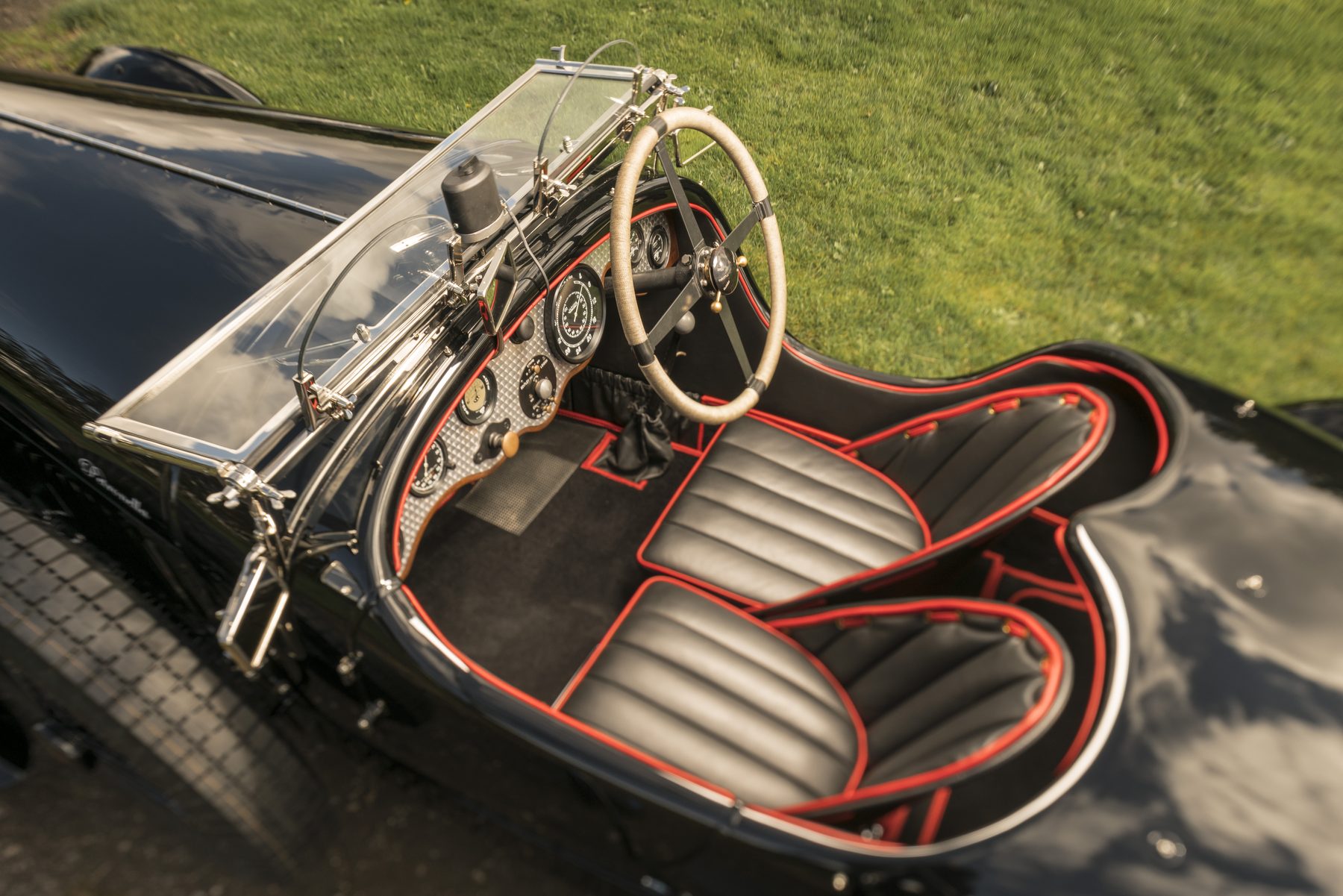 The cockpit from above: black leather seats with red piping, silver dash, cord-bound wheel