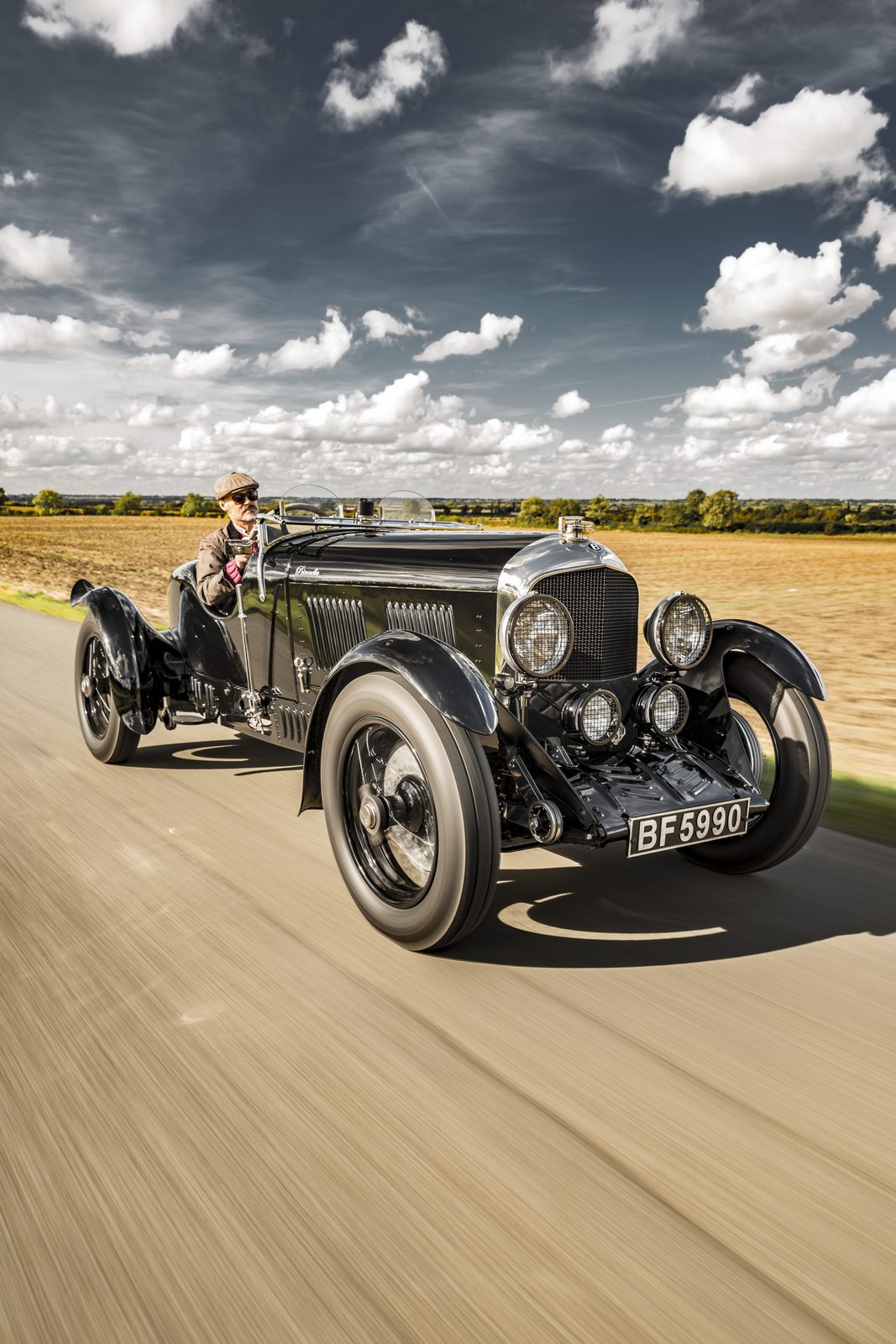 Petronella at speed on an open road between autumn fields, her driver in flat cap behind the aeroscreens
